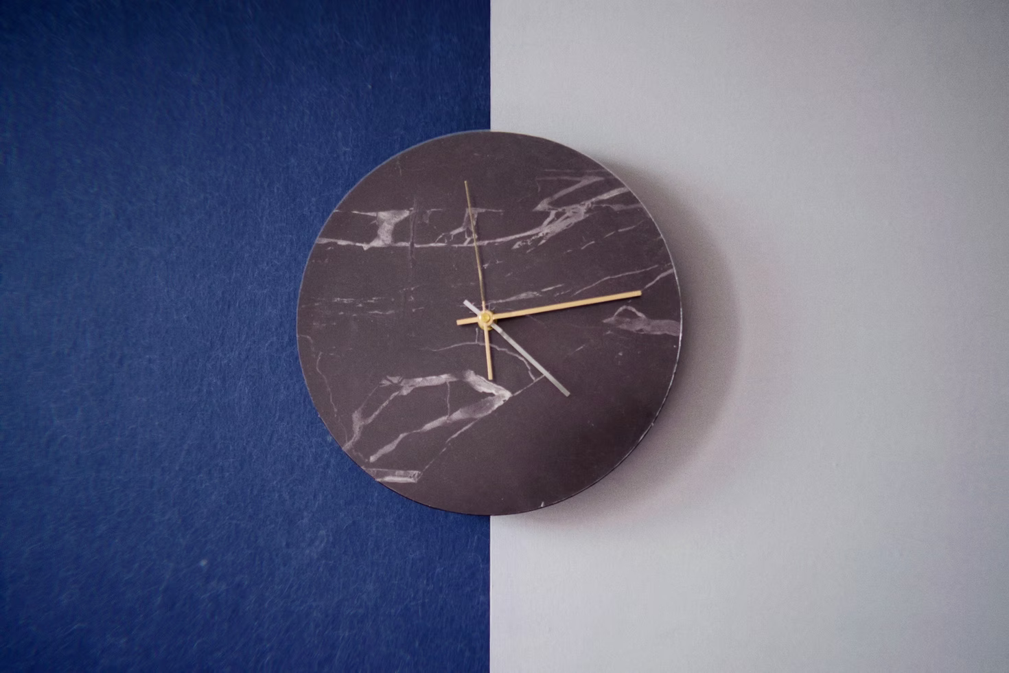 A gray clock with a marble face on a wall divided by blue and white paint.