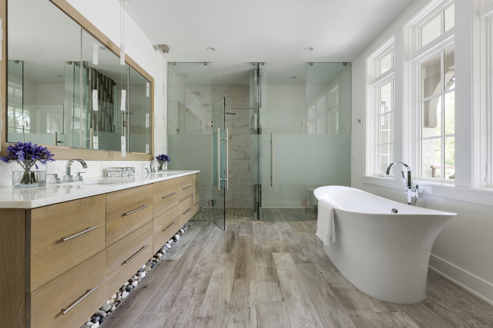 A bathroom with a double vanity, sauna, custom wood floors, and large windows