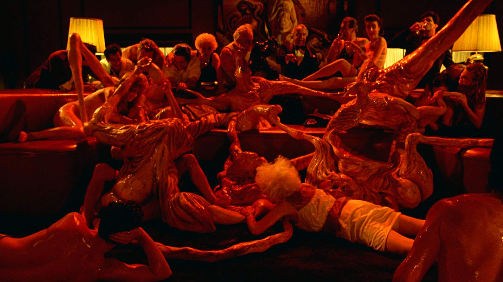 Society (1989). A grotesque scene illuminated in red light, what appears to be tangle of bodies, some of which look like masses of flesh and organs, slick with blood.