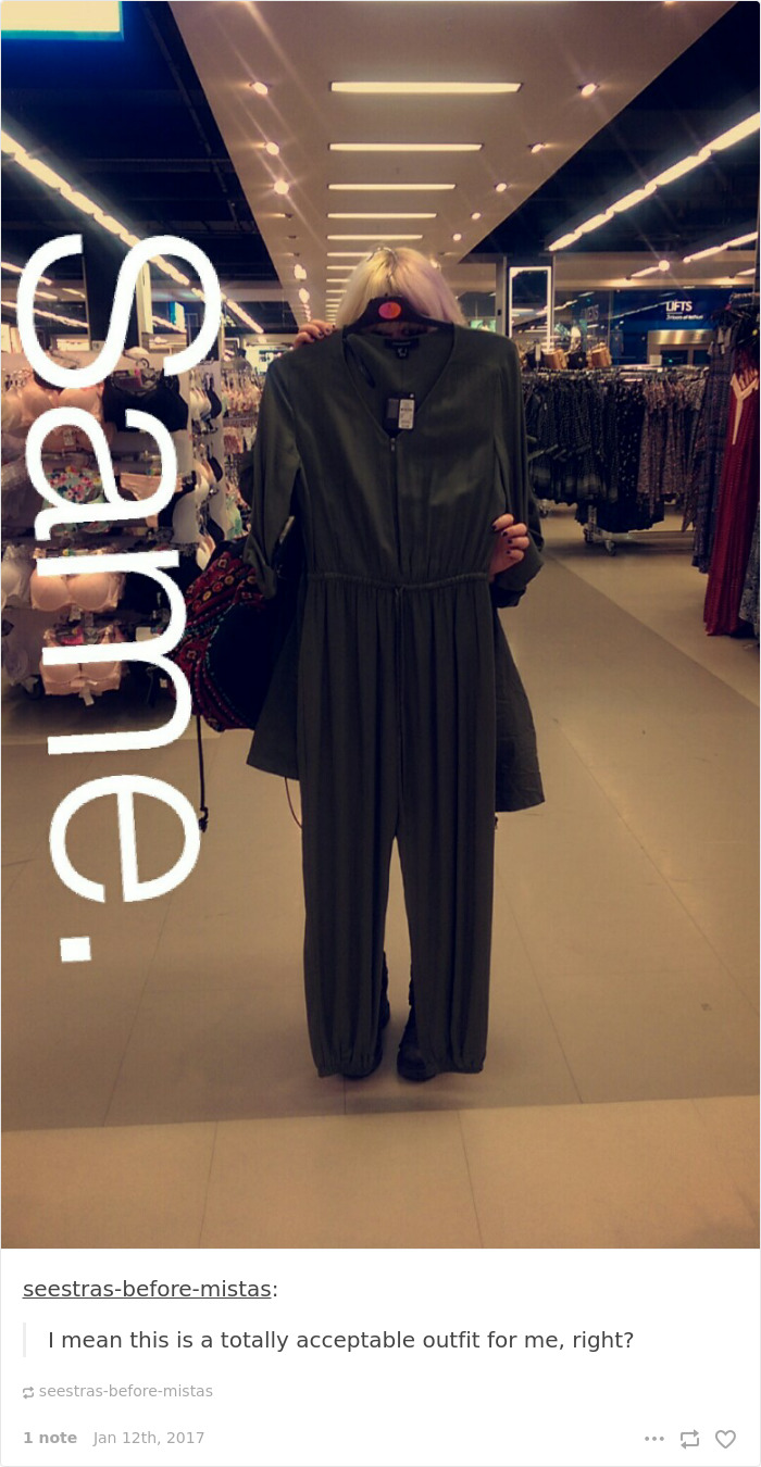 short girl at the mall holding a jump suit in front of herself in the mirror; however, the jumpsuit is taller than her