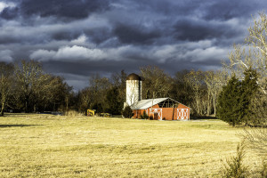 Red barn in a field of cut grass with storm clouds in the distance