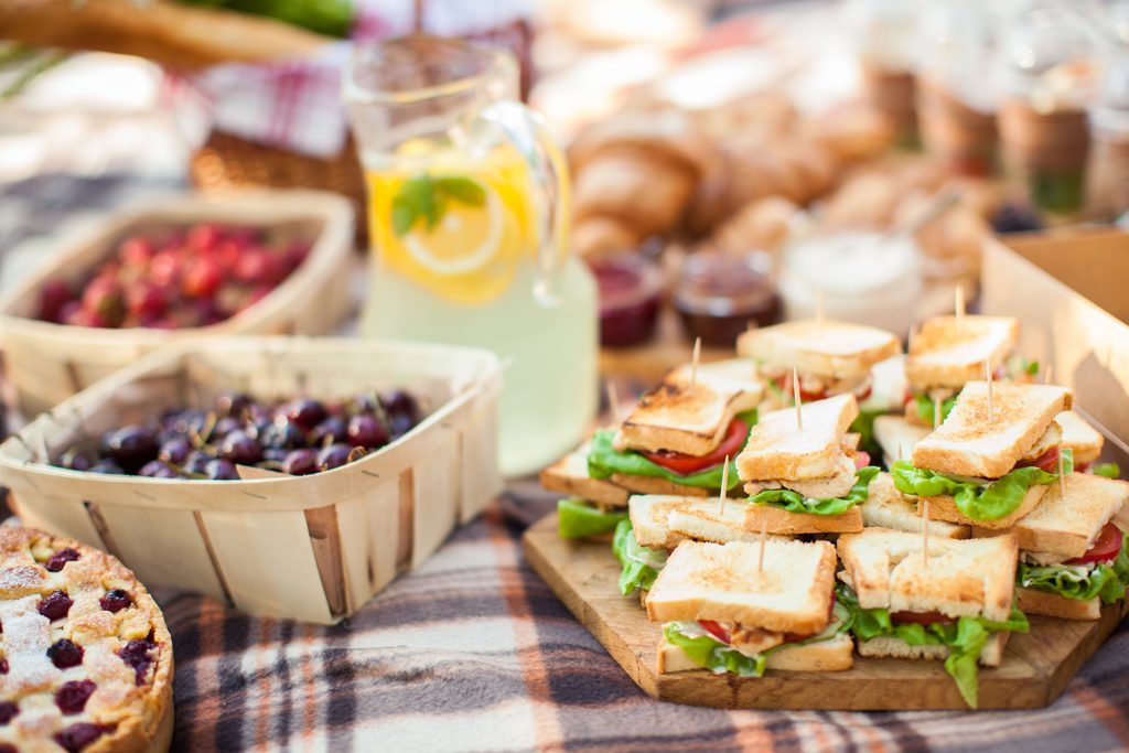 Finger food ideas for picnic, fresh mini sandwiches, fruits, tart and lemonade.