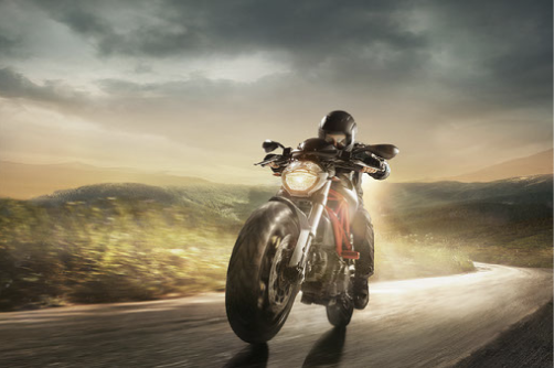 A solo motorcycle rider burning rubber and calories while on his motorcycle, driving through a cloudy dark sky. 