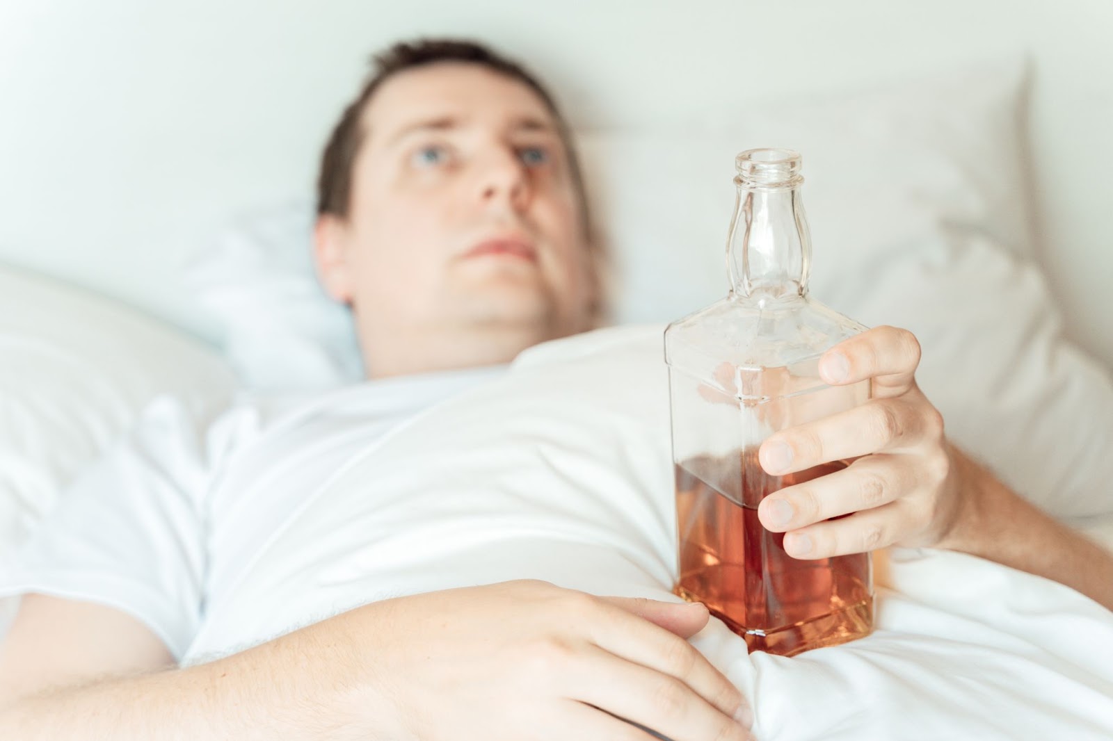 Man laying in bed with bottle of alcohol.