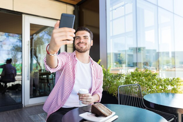A man taking a selfie while enjoying his coffee and dessert.
