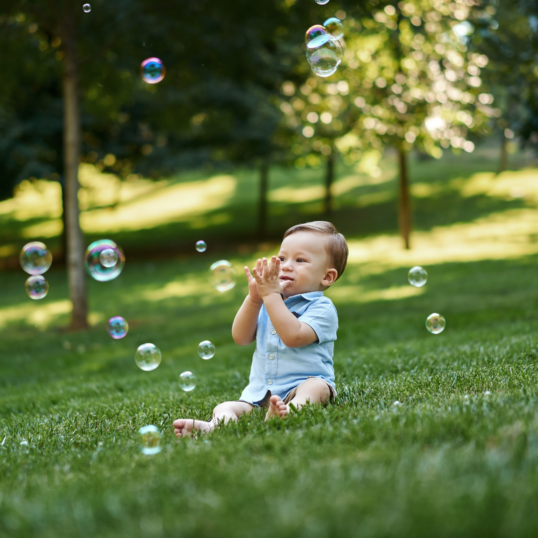 Baby sitting on the grass fascinated with bubbles outside the house