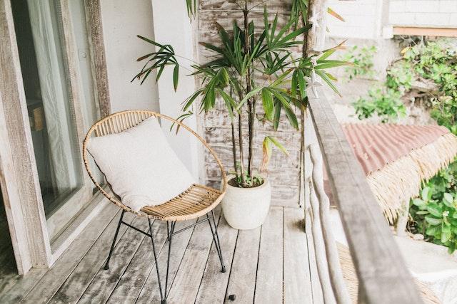 A balcony chair with a throw pillow placed next to a plant.