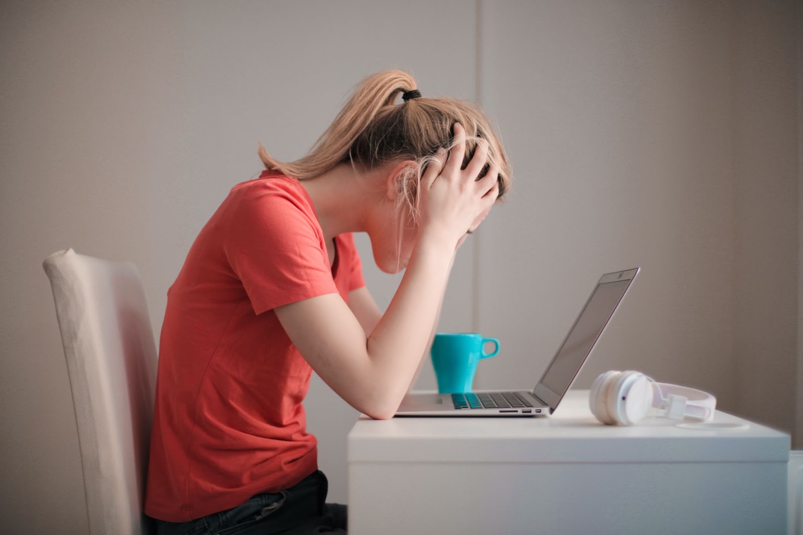 A girl sits hunched over a computer at a desk, looking stressed.