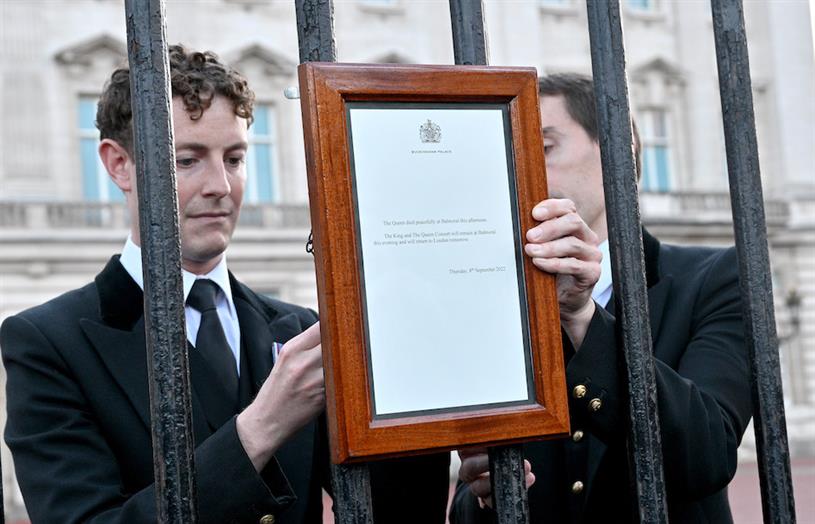 Two men putting a sign on the Buckingham Palace gate to announce the Queen's death