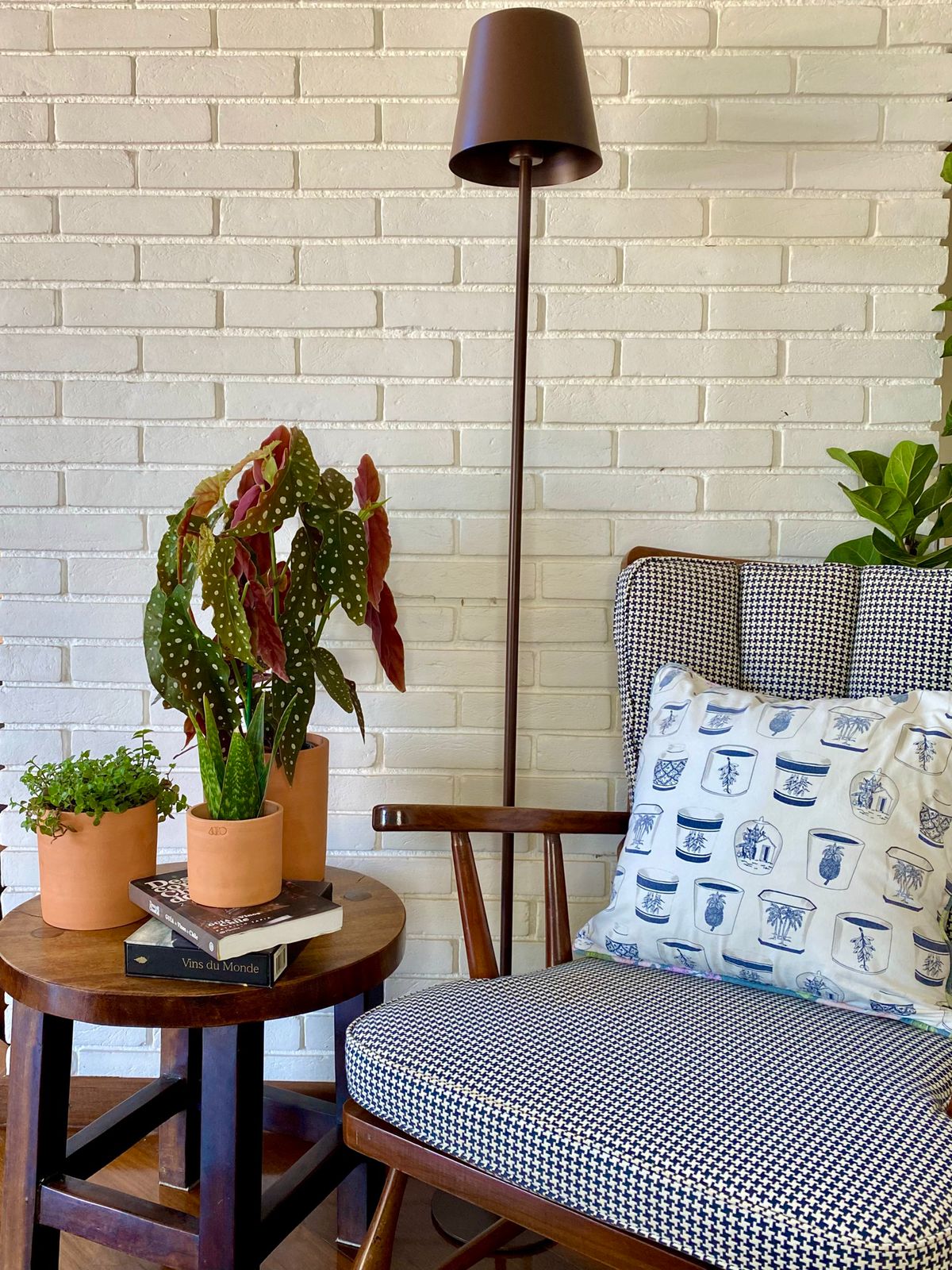 Cantinho de sala com mesa de madeira com composição de plantas pequenas e uma poltrona de madeira com estofado quadriculado