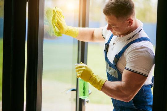 WeServe | a man wearing a white shirt and blue overalls and yellow gloves cleaning a window.