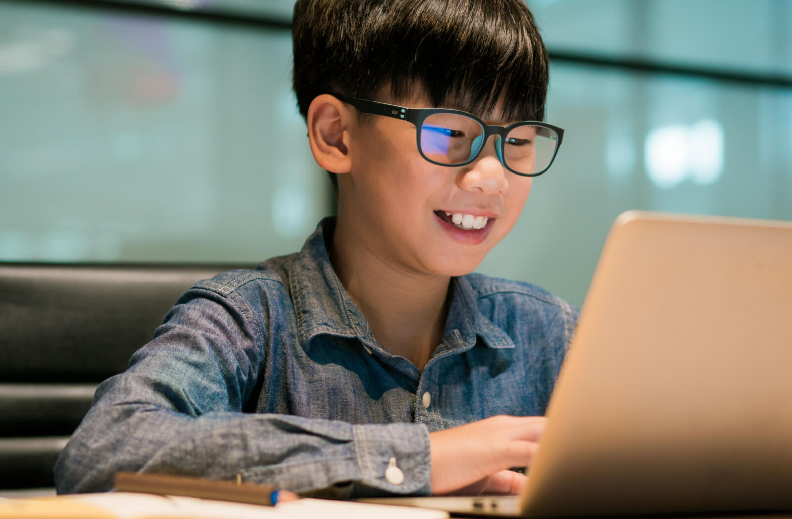 A boy is wearing blue-light eyeglasses to protect his eyes while he is on his computer.