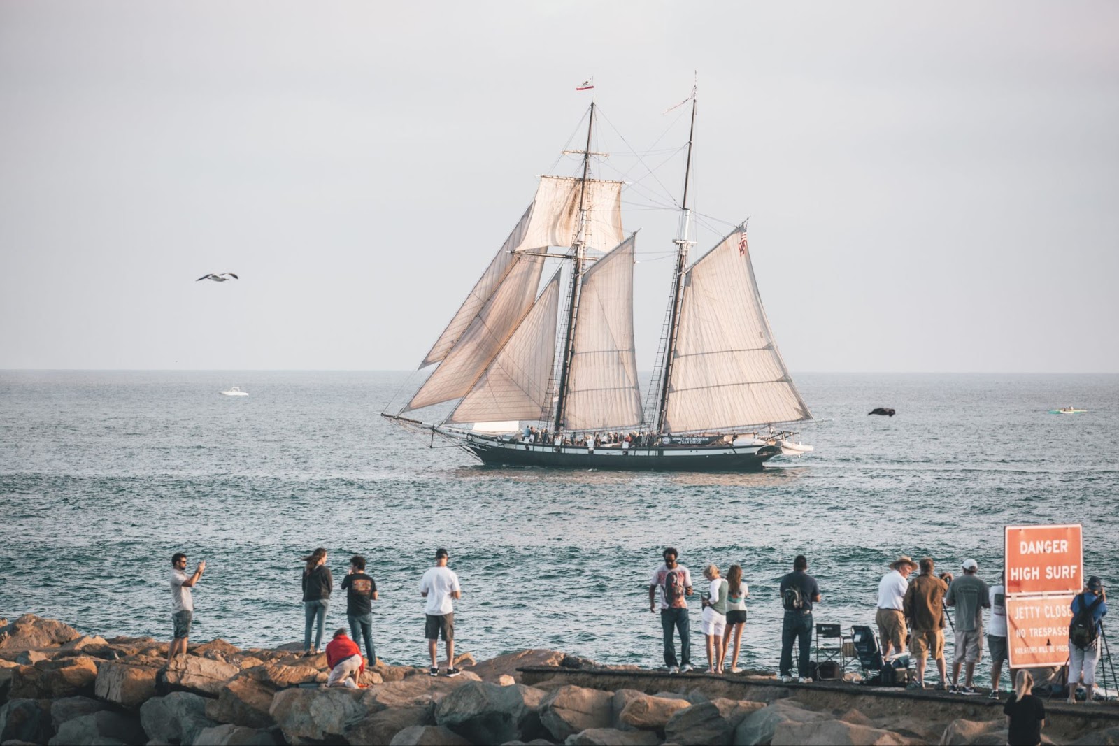 a group of people standing on a rocky shore next to a sailboat
