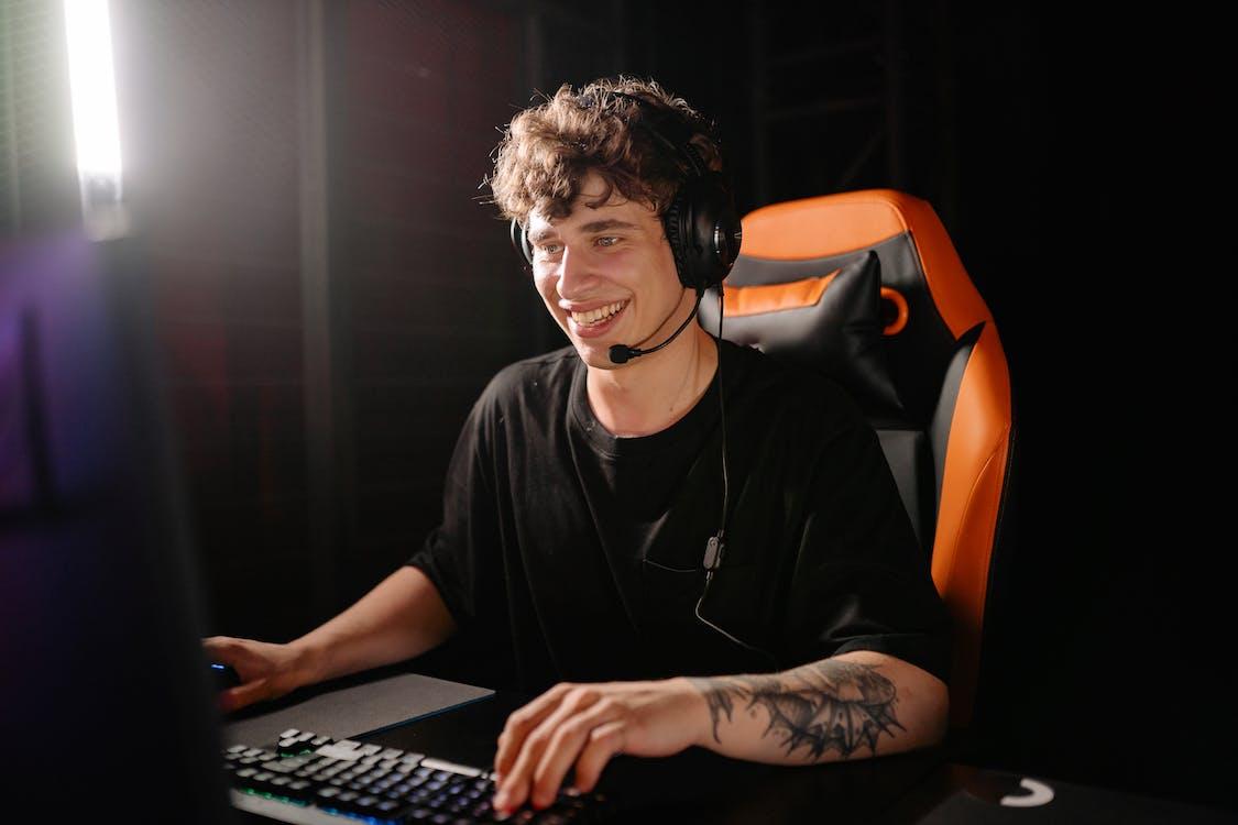 Free Photo of a Man in a Black Shirt Smiling while Playing on a Computer Stock Photo