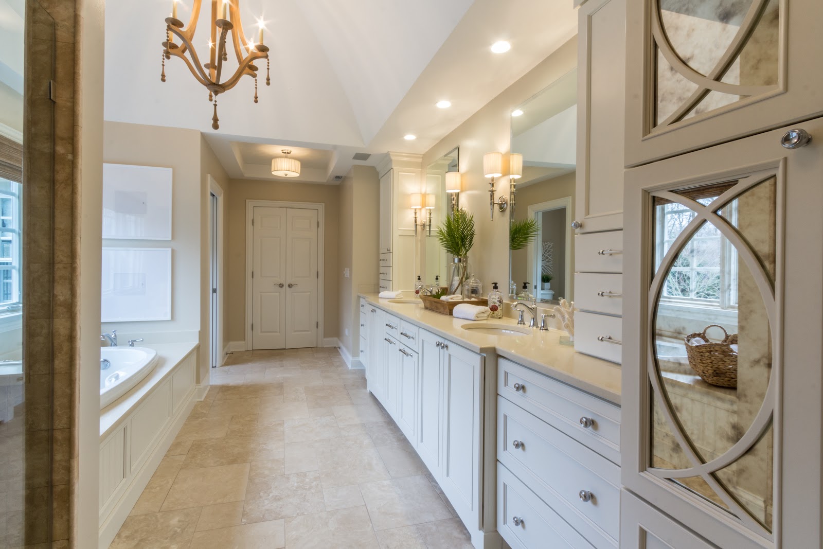 Elegant white transitional bathroom with mirrored cabinetry, dual sinks, a vaulted ceiling and chandelier.
