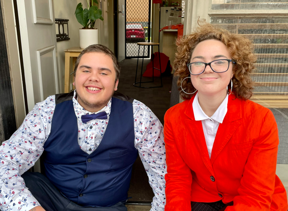 William smiling and sitting with Felicity who wears a bright red blazer