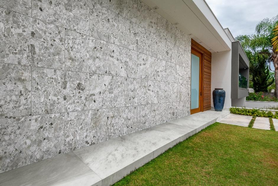 fachada de casa com revestimento de granilite em tom neutro nas paredes, gramado e porta grande de madeira.