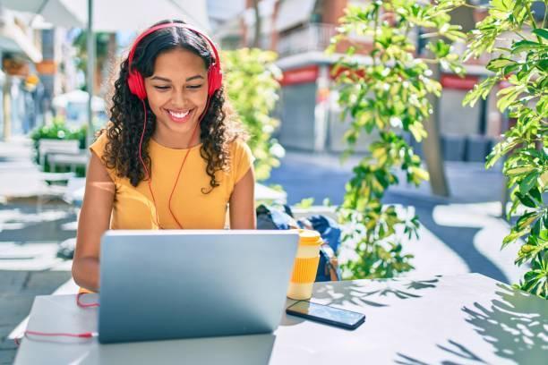 Young african american student girl using laptop sitting on the table at terrace. Young african american student girl using laptop sitting on the table at terrace. listening to music while working stock pictures, royalty-free photos & images