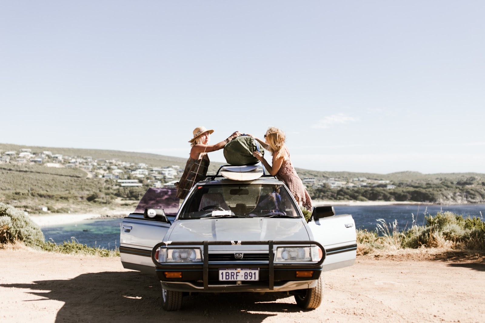 Two girls fixing the top of their car luggage to learn how to pack your car