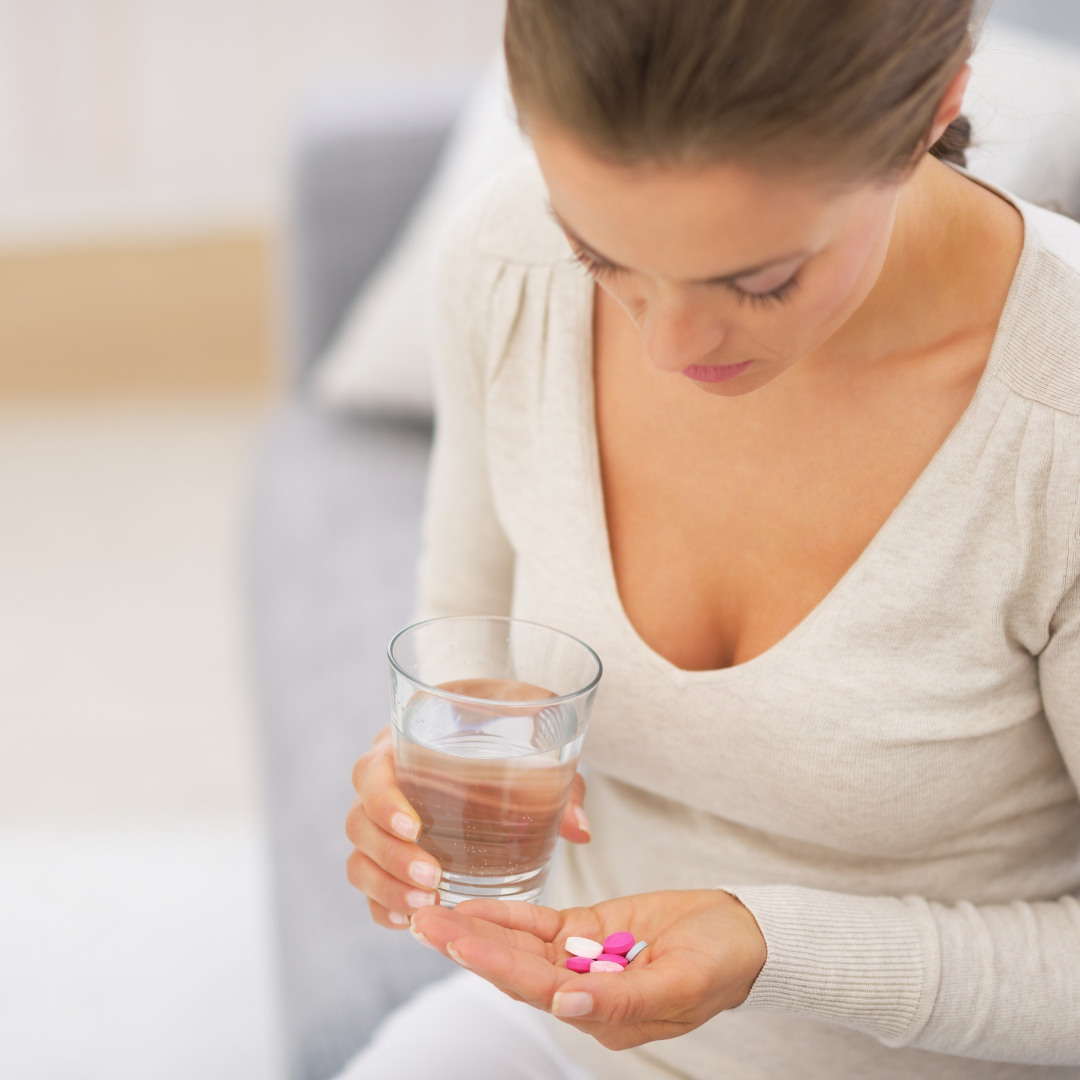 A lady holding pills with a glass of water wondering if it's safe.