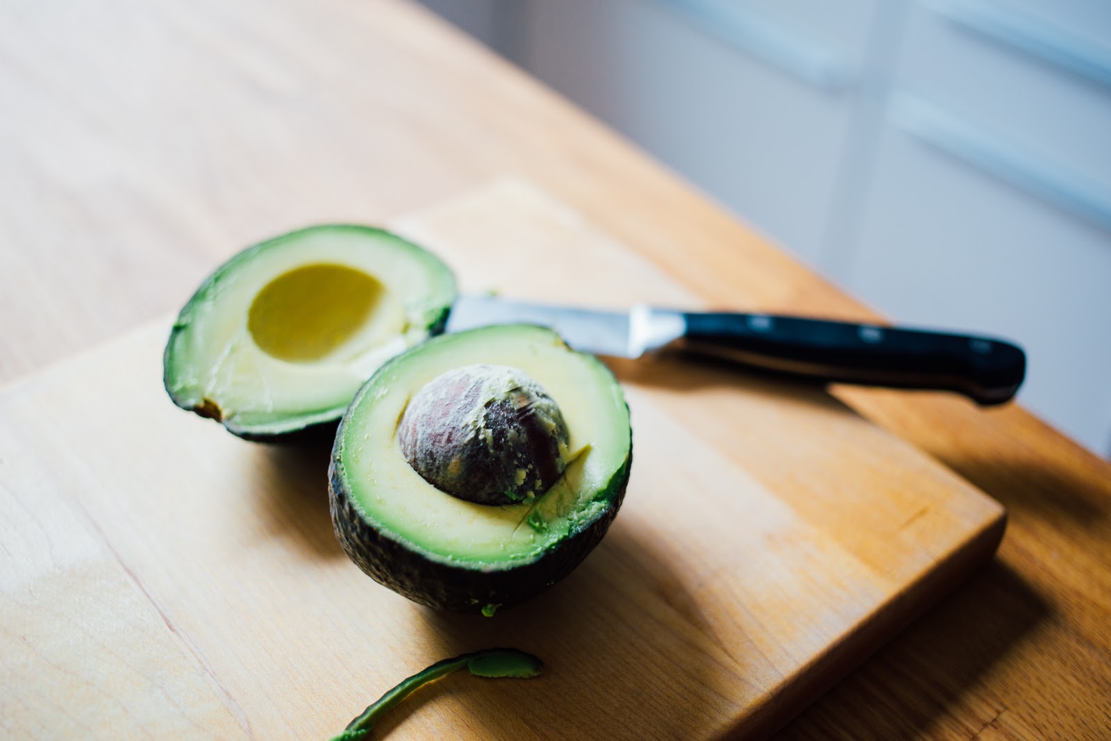 An avocado cut in half sitting on cutting board.