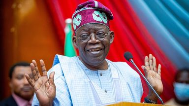 Ahmed Bola Tinubu on a podium with both hands raised 