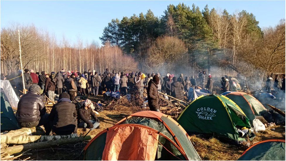 Photo of many people huddled around camp fires and lots of tents