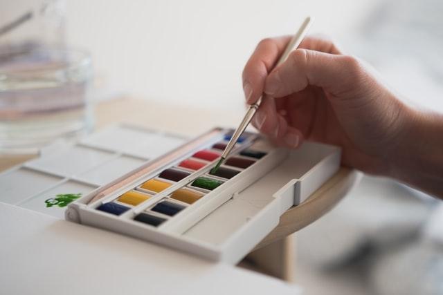Woman holding a paintbrush and dipping it in watercolors
