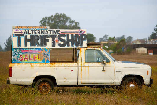 White truck with signs on the back that say "Alternative Thrift Shop" and "Sale."