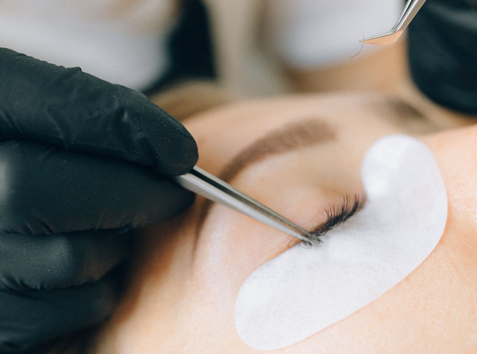 An eyelash technician carefully applies eyelashes to client's eye.