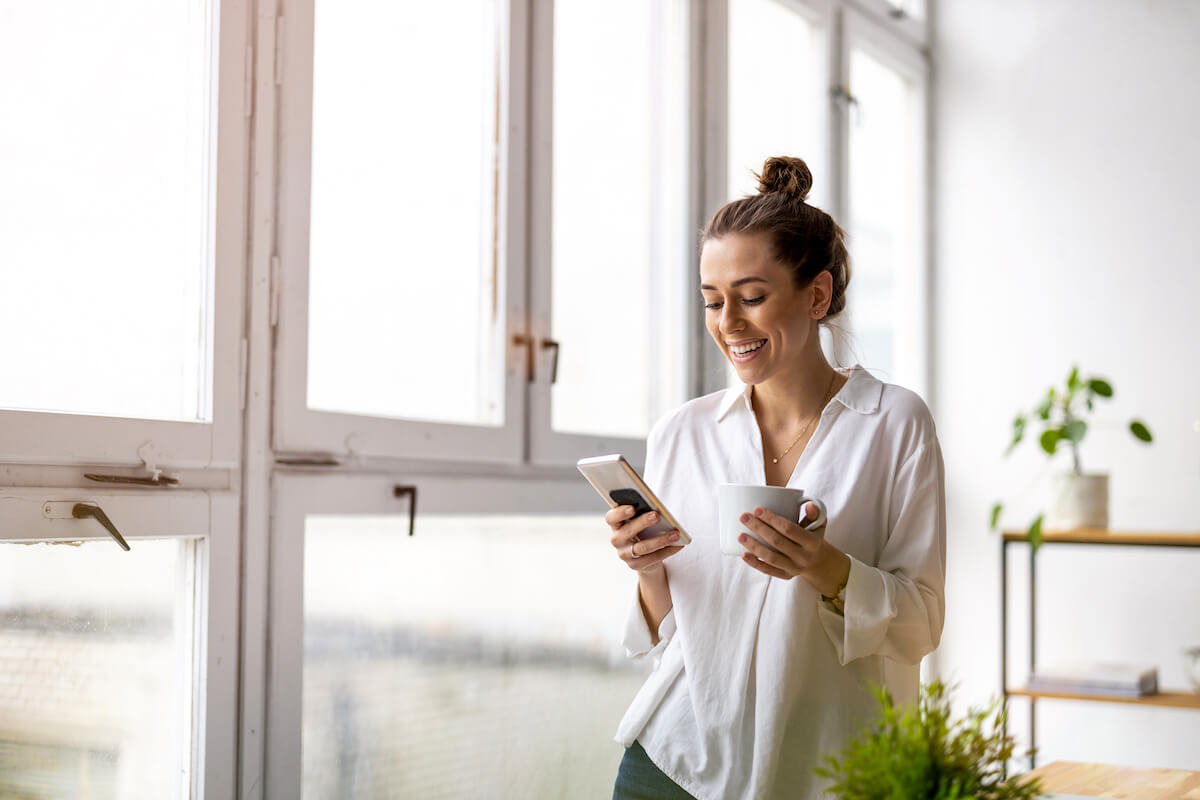 Employee engagement ideas: woman happily using her smartphone while holding a cup of coffee