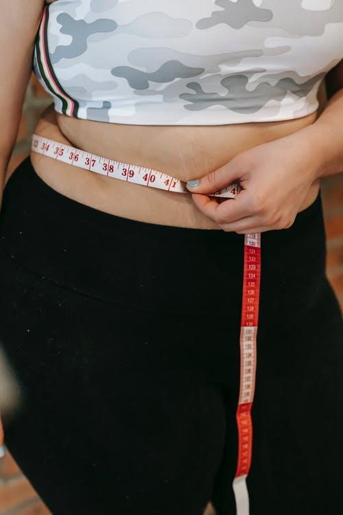 Plus size woman using measuring tape on belly