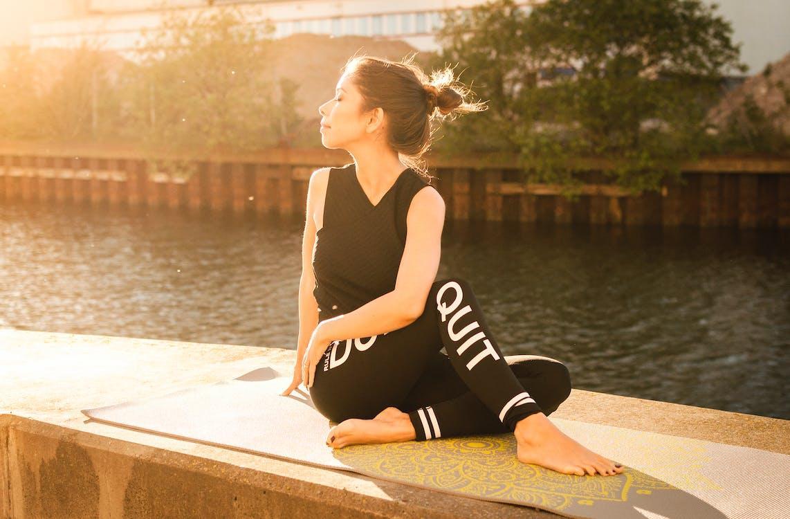 Free Woman Wearing Black Fitness Outfit Performs Yoga Near Body of Water Stock Photo