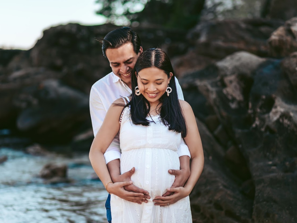 Maternity shoot of a couple in white outfit on a beach
