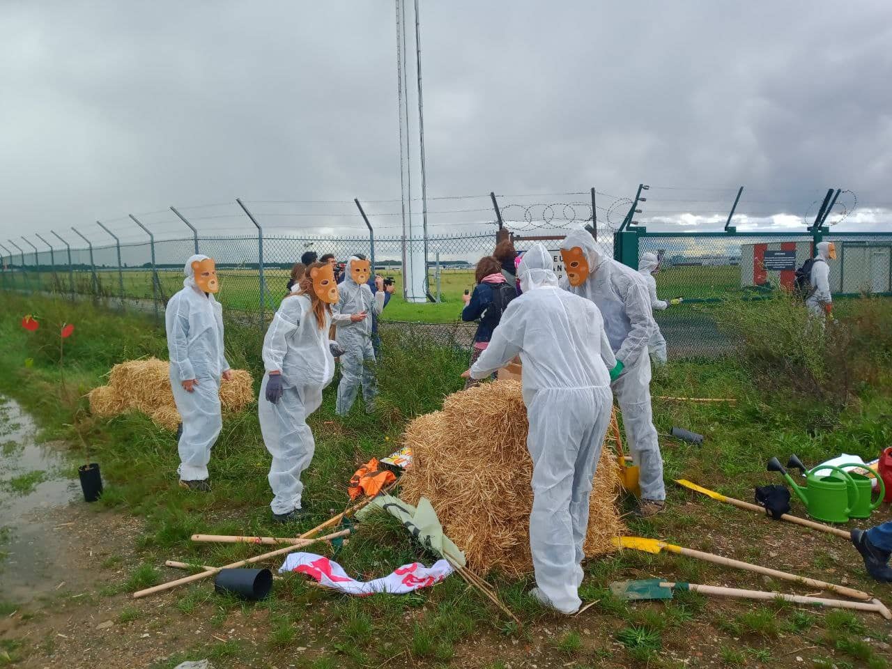 rebels in white overalls and animal masks carry hay bales into the airport runway
