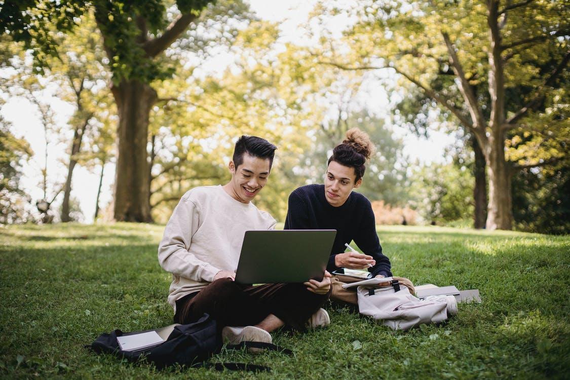 Free Man and Woman Sitting on Green Grass Field Using Laptop Computer Stock Photo