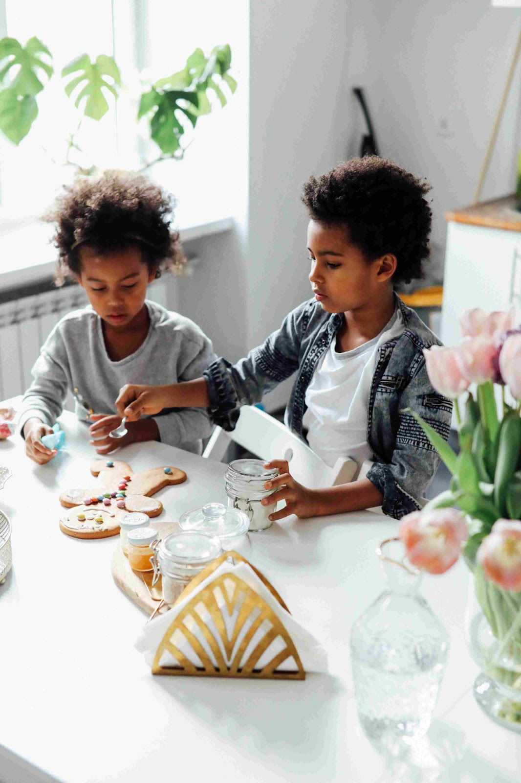 Two young children sitting at a table decorating a gingerbread man cookie