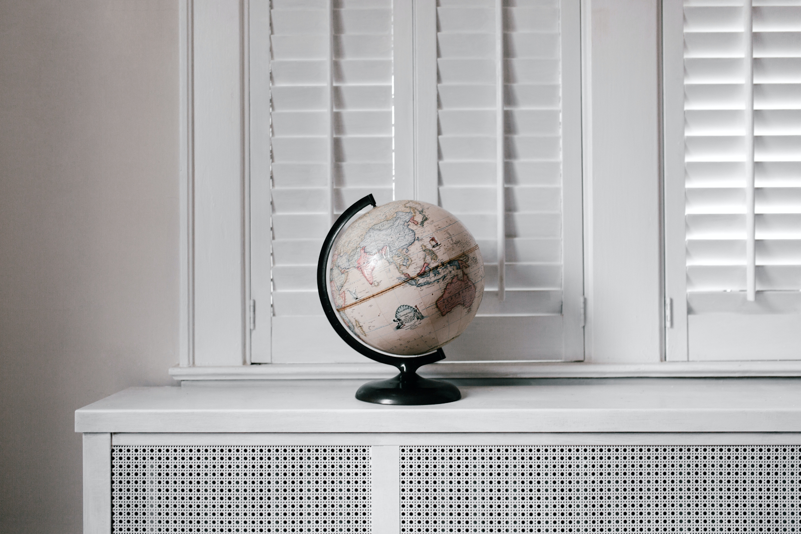 Globe with a black stand sitting on a white shelf with a window with closed blinds in the background.