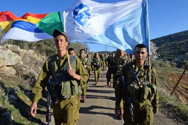 Soldiers of the Herev Battalion in a beret march holding up the battalion’s flag and the official Druze flag. 