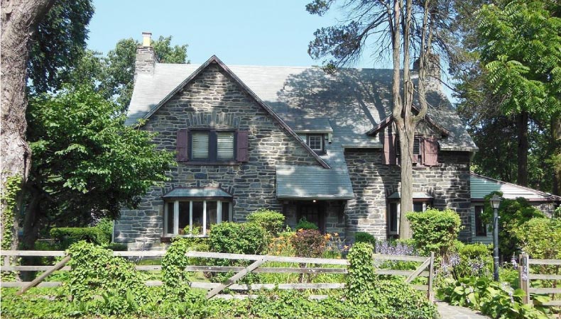 A stone colonial home in Ardmore, Pennsylvania. Trees cast shadows on the house and vines creep up fences.