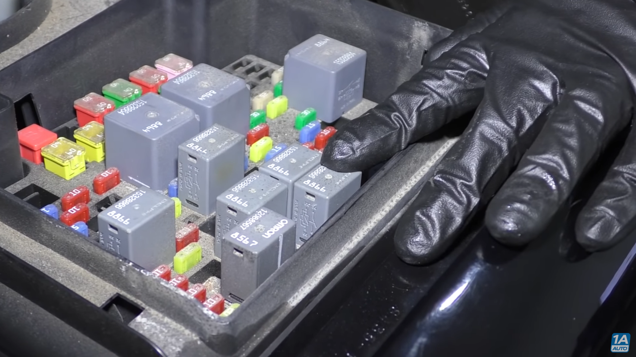 Mechanic pointing to a relay switch inside the fuse box.