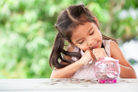 Cute asian little child girl stingy her money and saving money in piggy bank for the future