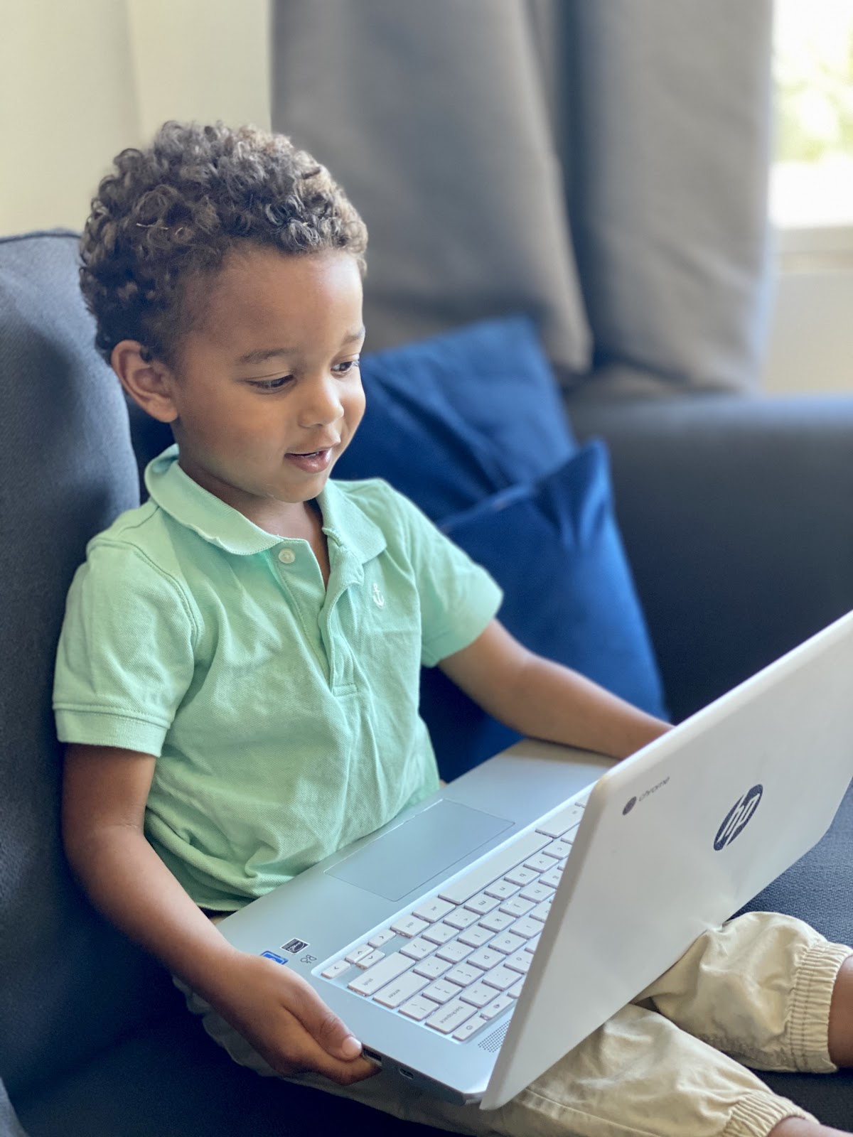 A little boy sits on a couch holding a computer while playing with the Homer reading app