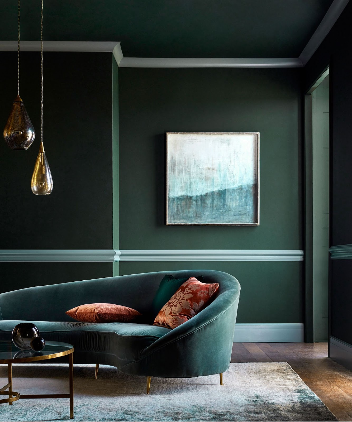 Dark green living room with a curved velvet sofa, abstract artwork, and modern lighting fixtures.