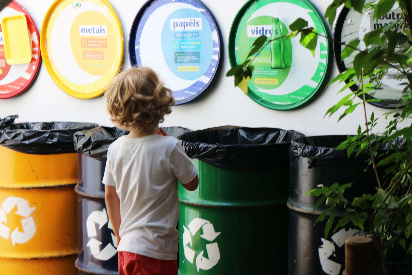 A imagem mostra uma criança em frente a latas de lixo reciclável.