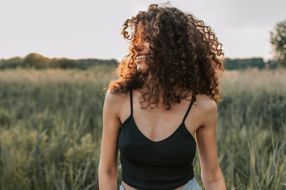 A woman standing in a field with sunlight on her face, and smiling.