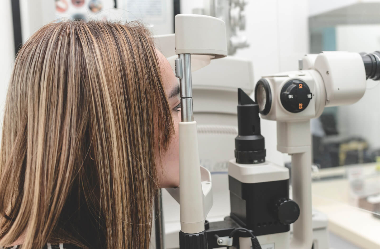 A woman is undergoing an eye test via an autorefractor to measure her eye's refractive error.