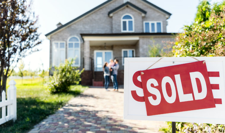 A family standing in front of their new home with a sold sign in front