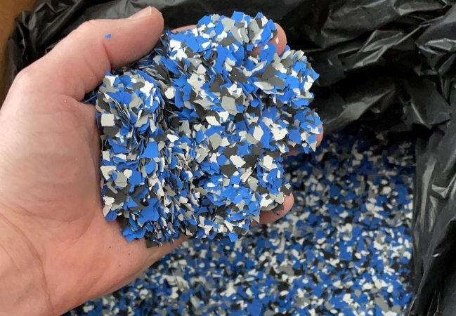 A person is holding a handful of blue, gray, and black decorative vinyl flakes used in epoxy flooring.