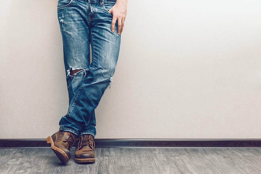Young fashion man's legs in pair of old jeans and boots on wooden floor.